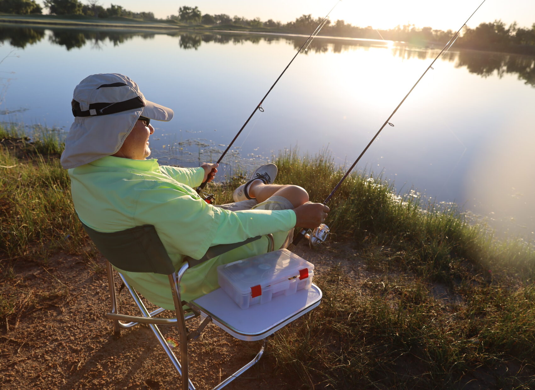 Person in a hat fishing by a serene lake at sunrise