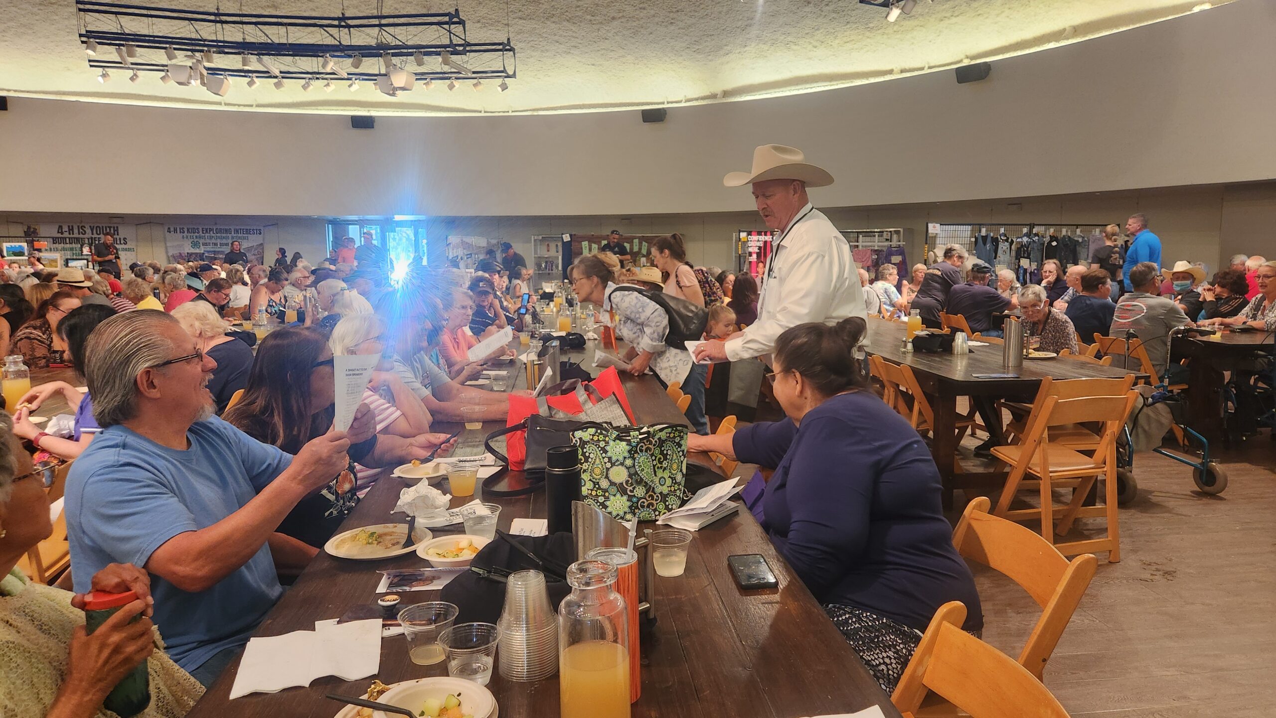 Crowded community event with people socializing and a man in a hat interacting with attendees.
