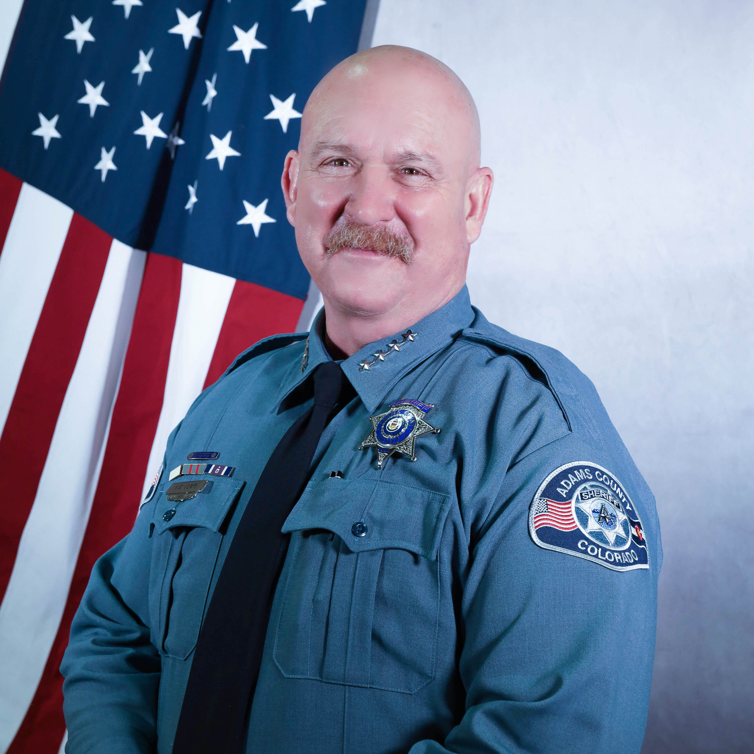 Sheriff Gene Claps in uniform standing in front of the American flag