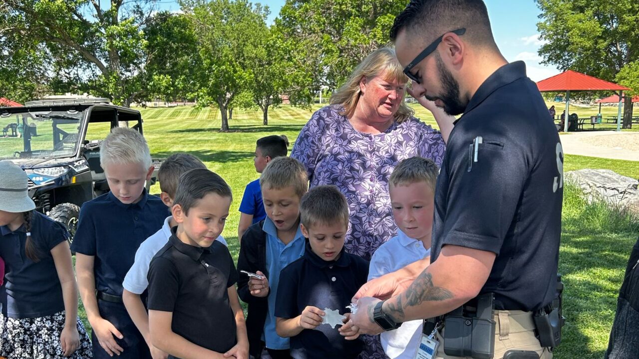 Children gather around a man in uniform showing an object outdoors.