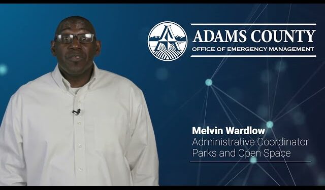 Melvin Wardlow, Administrative Coordinator, stands beside Adams County Office of Emergency Management logo.