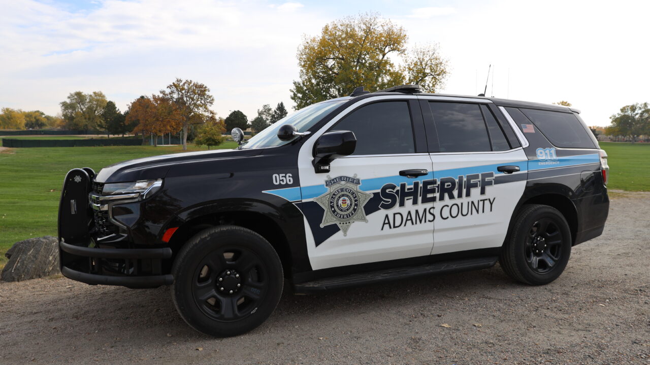 Adams County Sheriff patrol vehicle parked on gravel near green field.