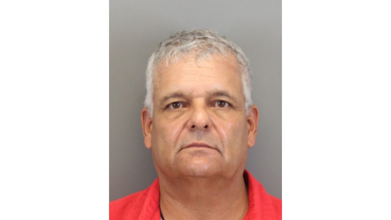 Reynaldo-Charles.png: Man with short gray hair and a serious expression wearing a red shirt.