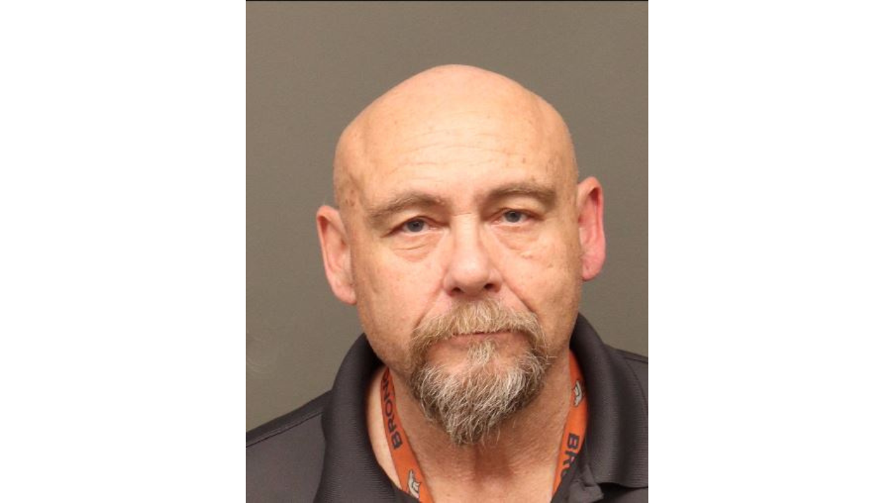 Troy Webb with neutral expression, wearing a brown lanyard, bald and bearded.