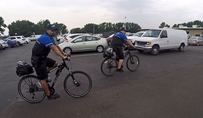 Two Adams County Sheriff Bike Unit officers on bicycles patrolling a parking lot with aparked cars.