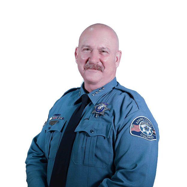 A man in a blue police uniform, smiling, wearing an Adams County badge.
