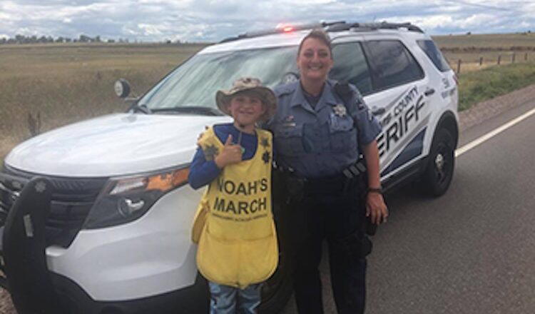 Boy in "Noah's March" apron smiling with sheriff beside sheriff vehicle.