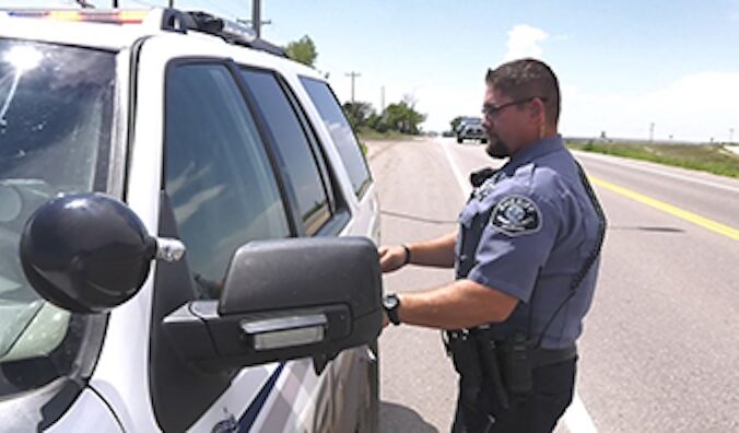Police officer standing next to patrol car on rural road.