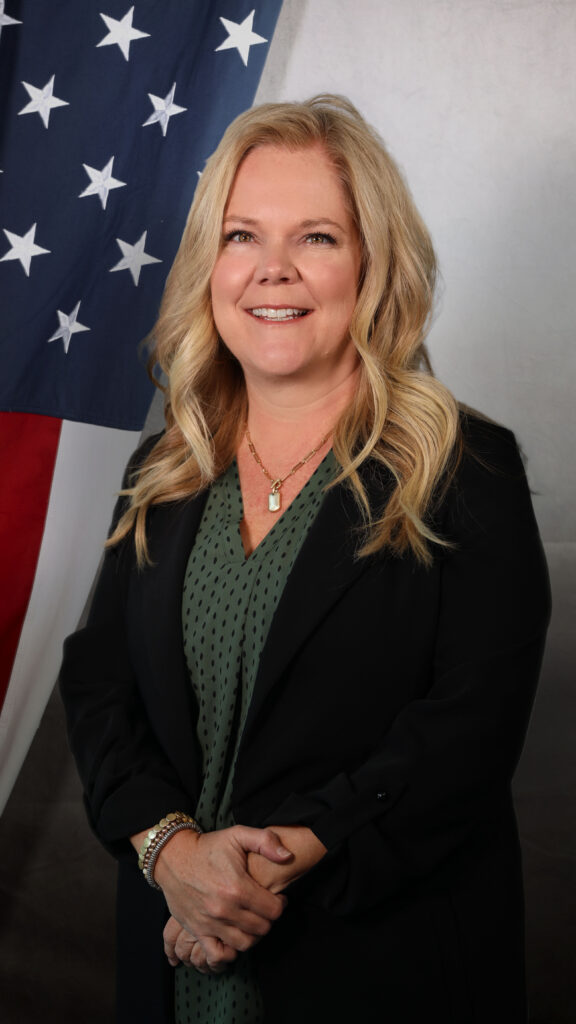 Jennifer Baessler, Human Resources Director at the Adams County Sheriff's Office, smiling in front of an American flag backdrop.