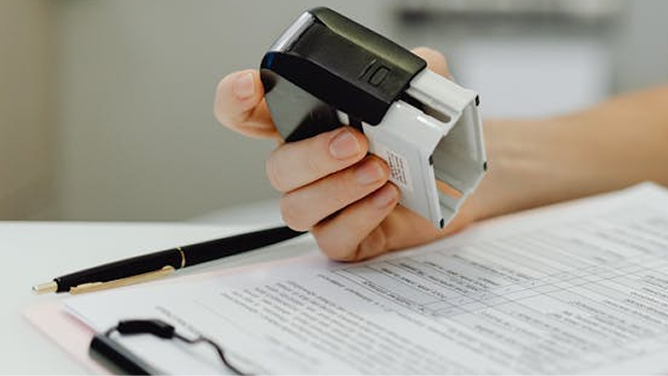 Hand holding a stamp over a document with text, pen nearby