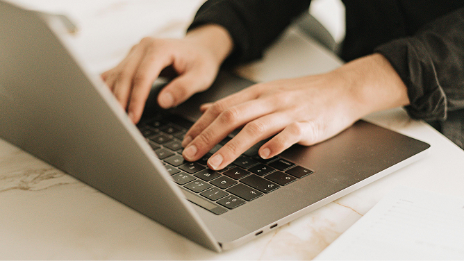 Hands typing on a laptop keyboard, on a marble table
