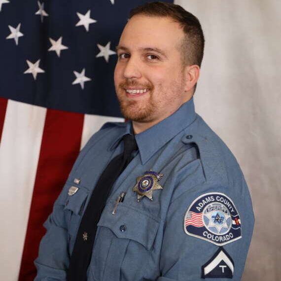 Sr. Deputy Martinez in uniform smiling, American flag in the background, Adams County patch visible.