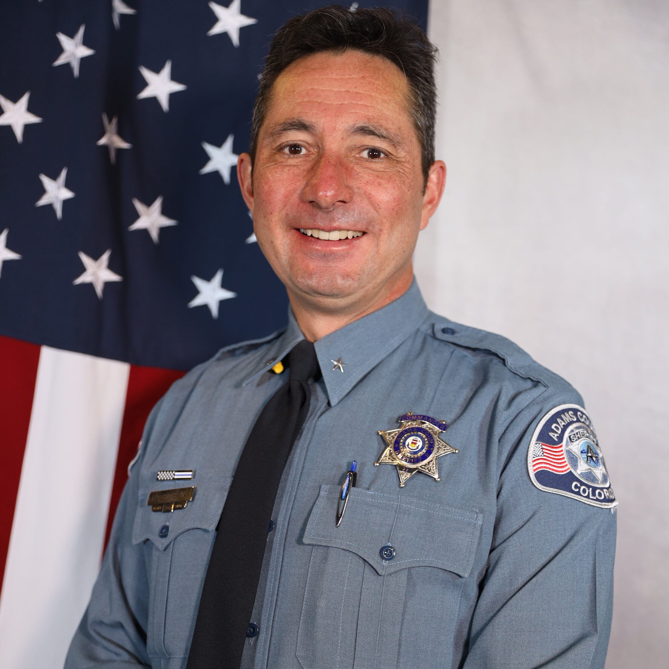 Bitterman-John smiling in uniform, standing in front of the American flag.