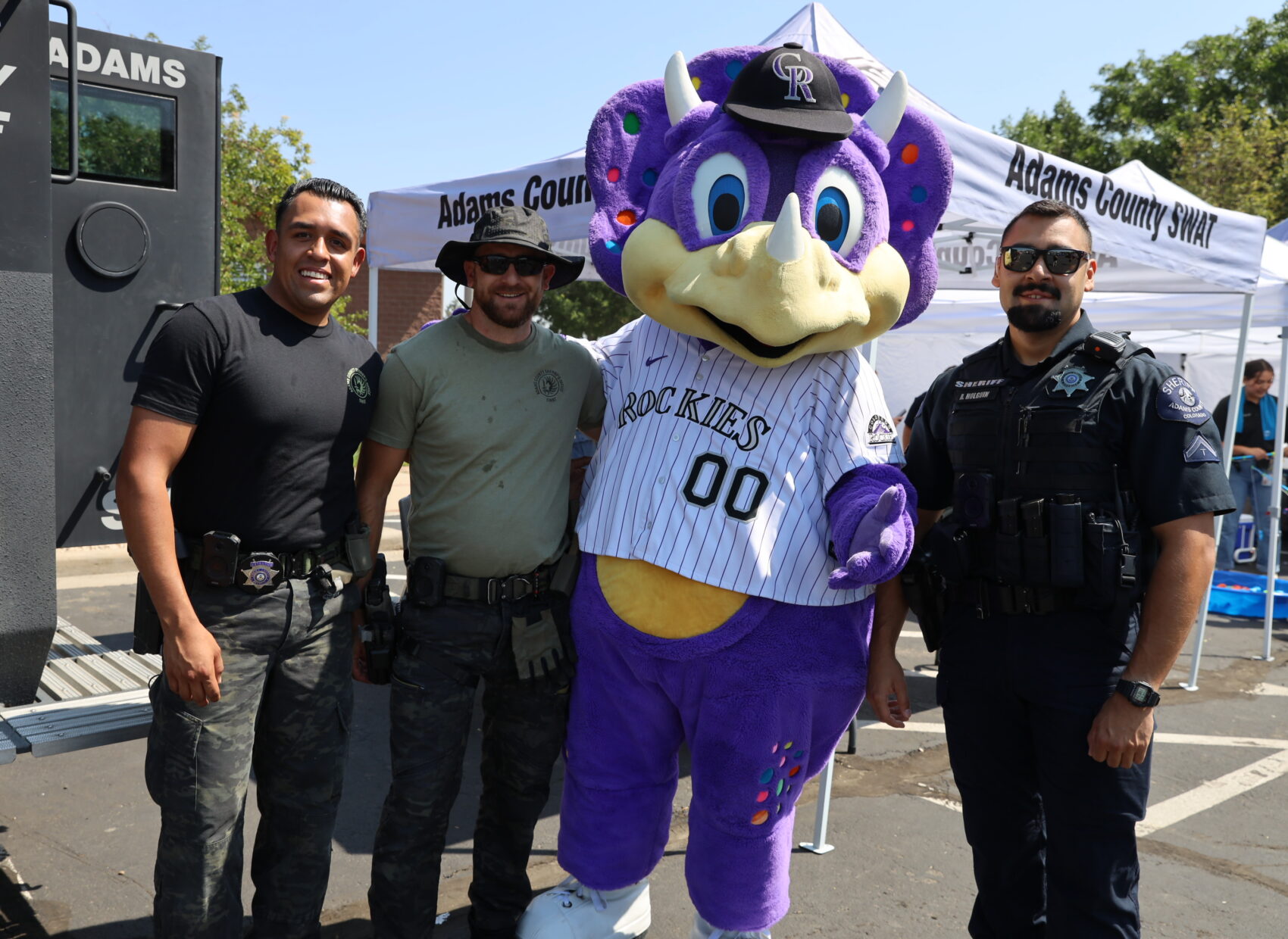 Dinger mascot with three Adams County law enforcement officers outdoors at an event