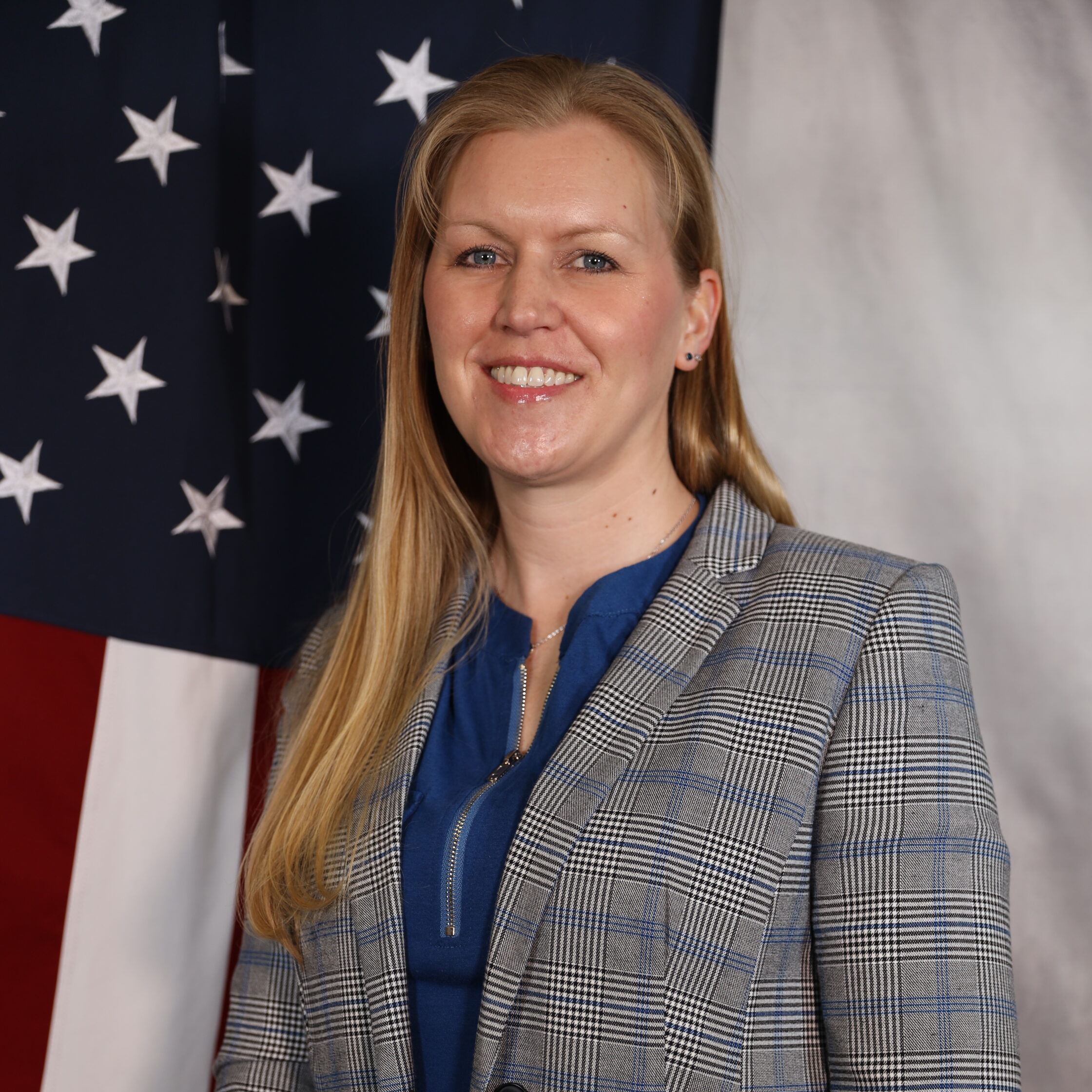 Lindsay Laughery smiling in front of a U.S. flag, wearing a plaid blazer and blue top.