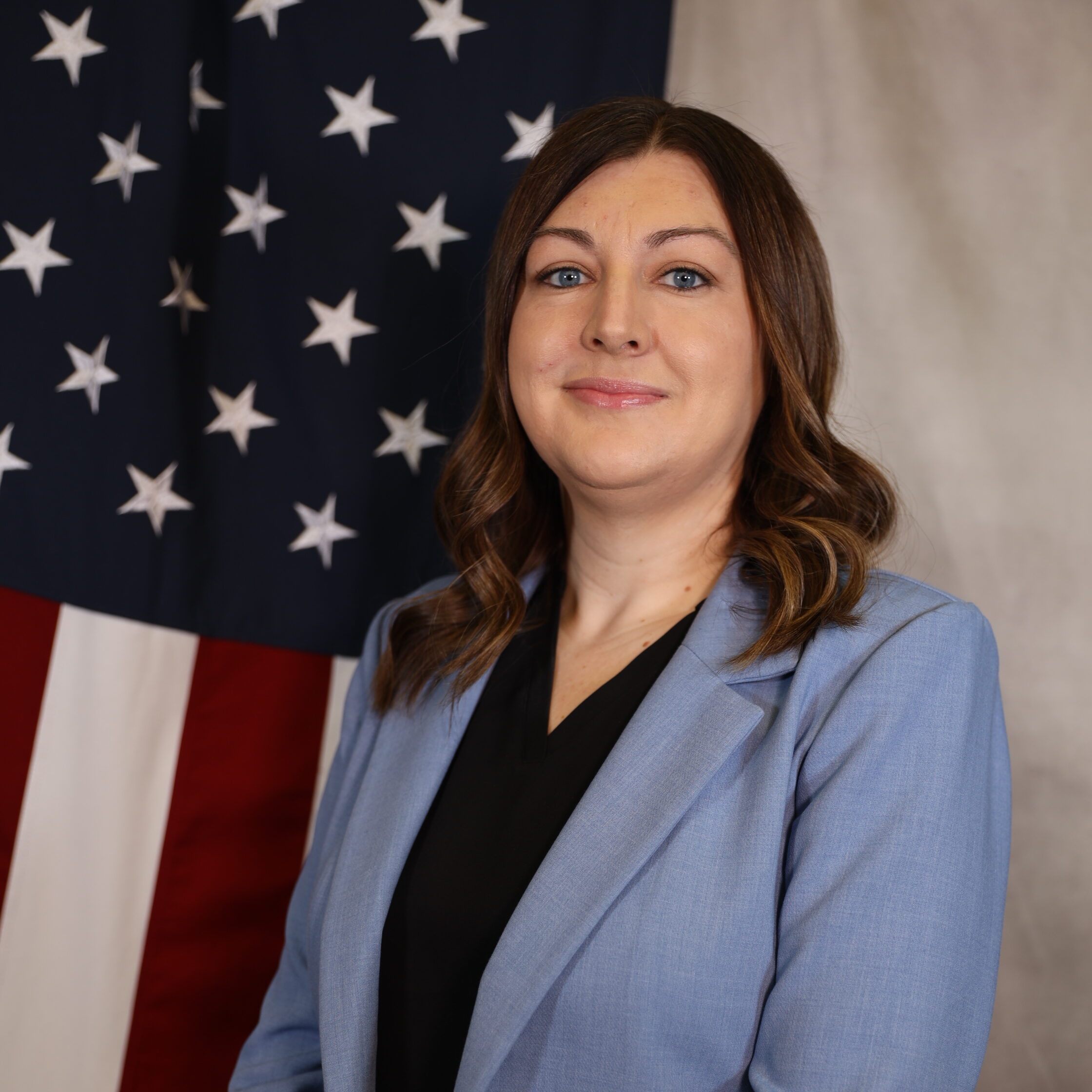 Sarah Manzanares in a blue blazer, standing before a U.S. flag.
