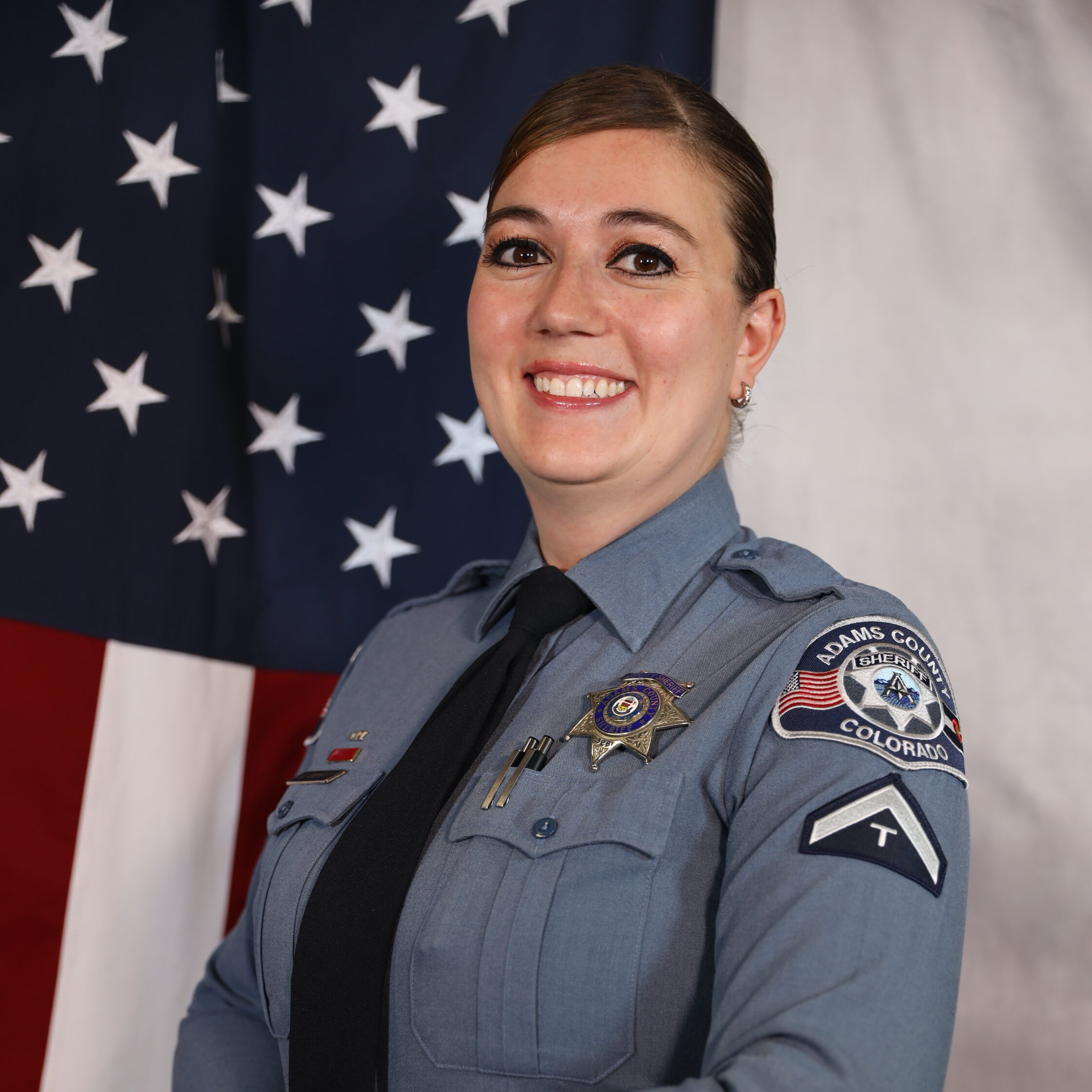 Overmyer-Jennifer in police uniform smiling, standing before an American flag.