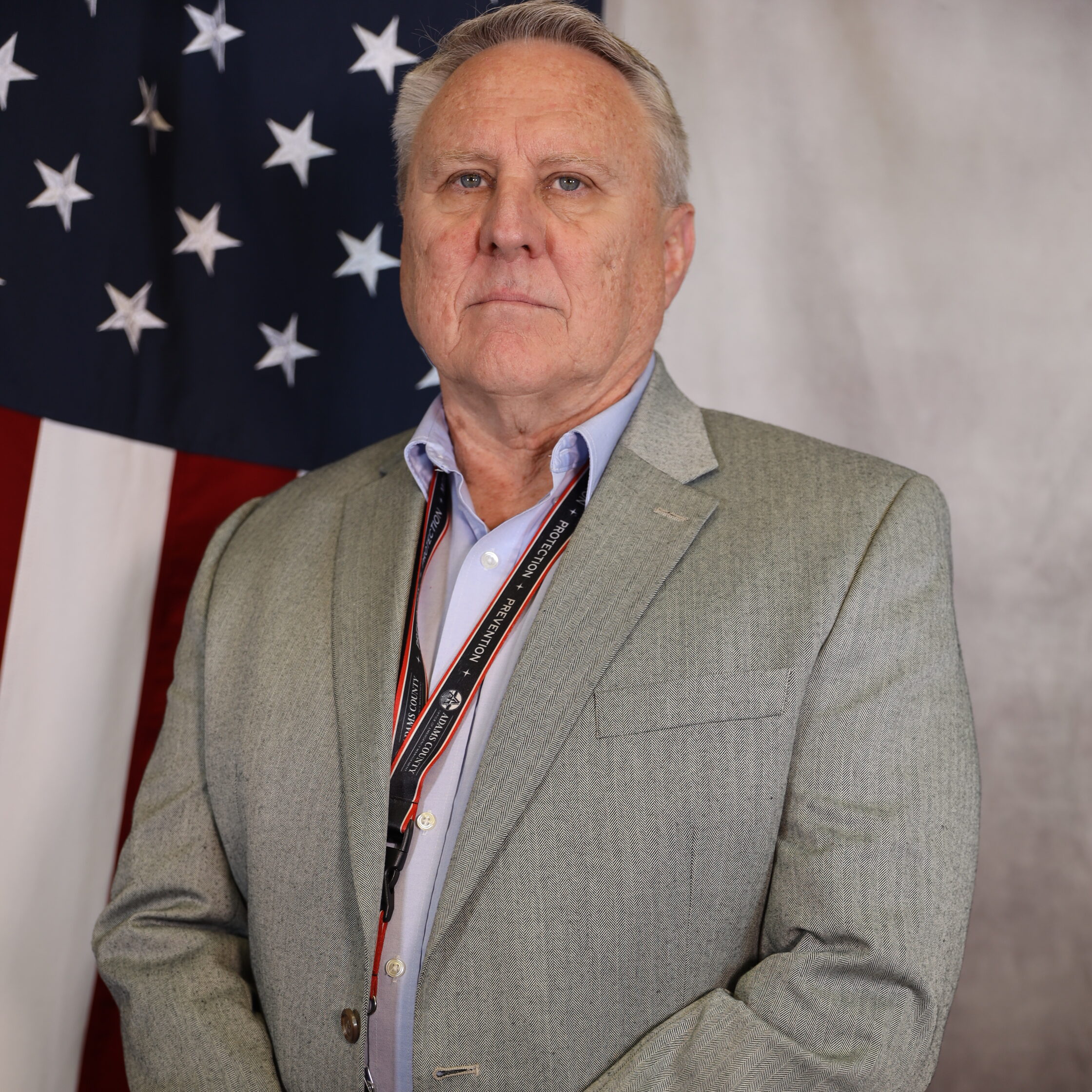 Sigman-Ronald standing in front of the American flag, wearing a gray suit.