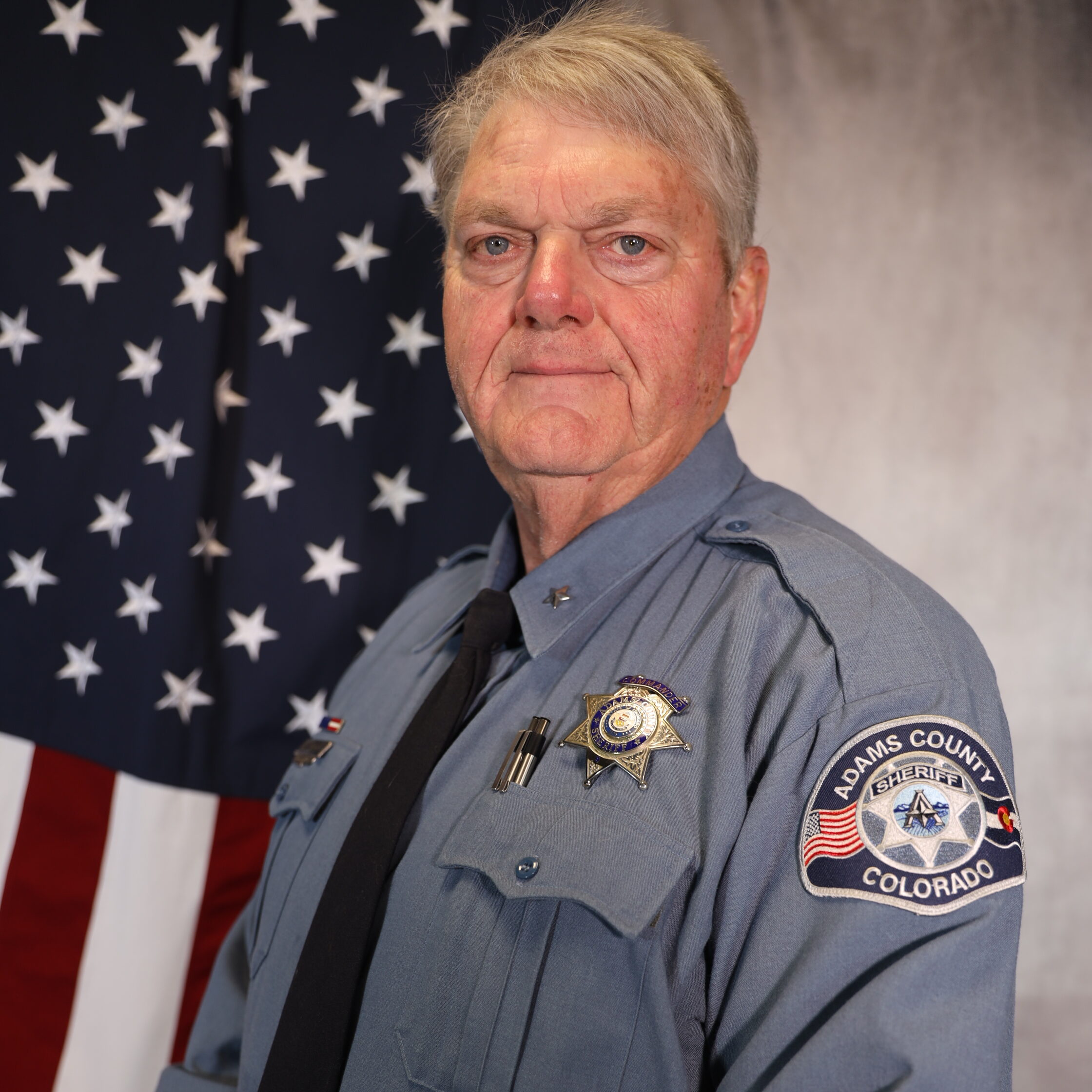 Smalley-Karl in uniform with Adams County Sheriff badge, standing before American flag
