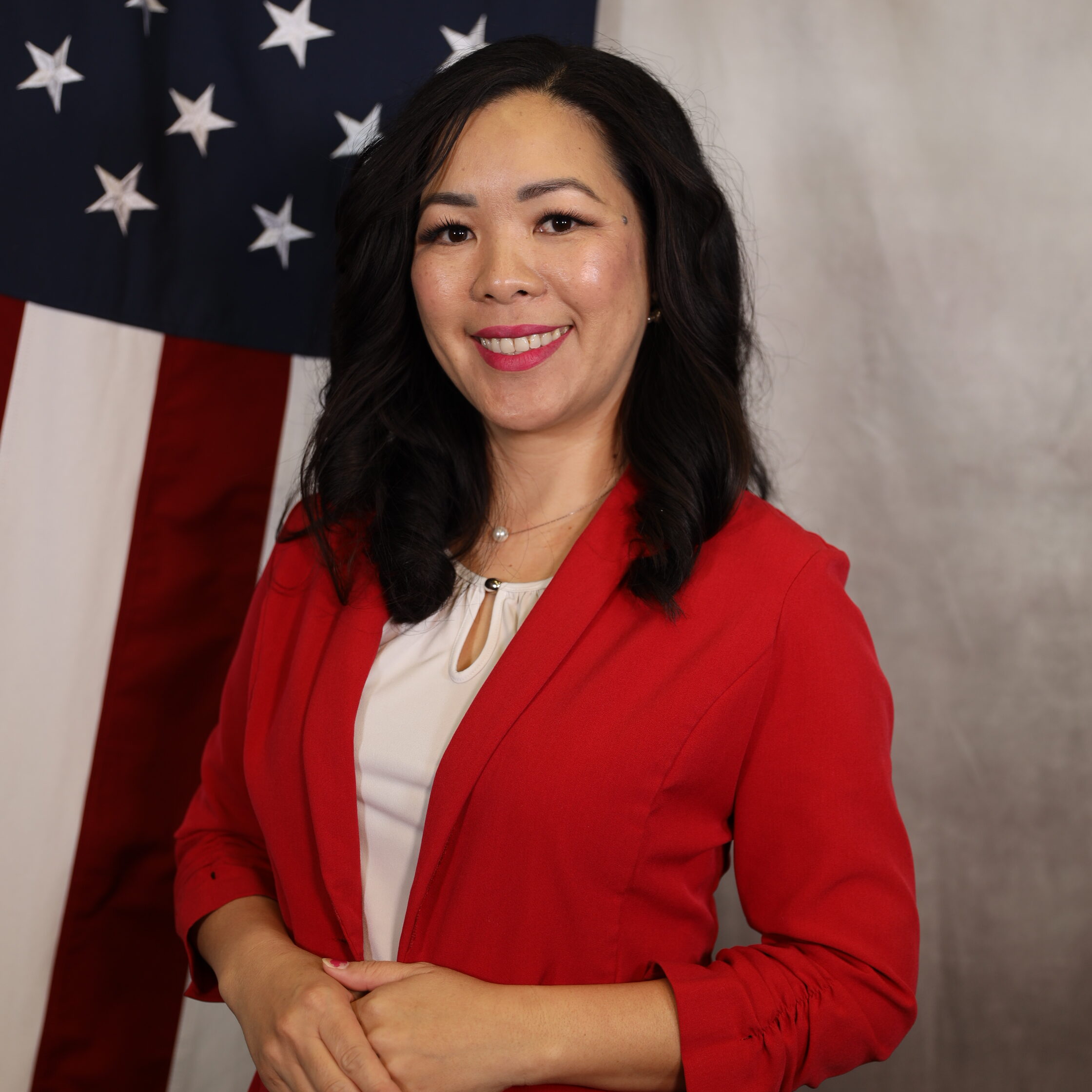 Yang-Trace.jpg: Woman smiling in red blazer, standing in front of American flag