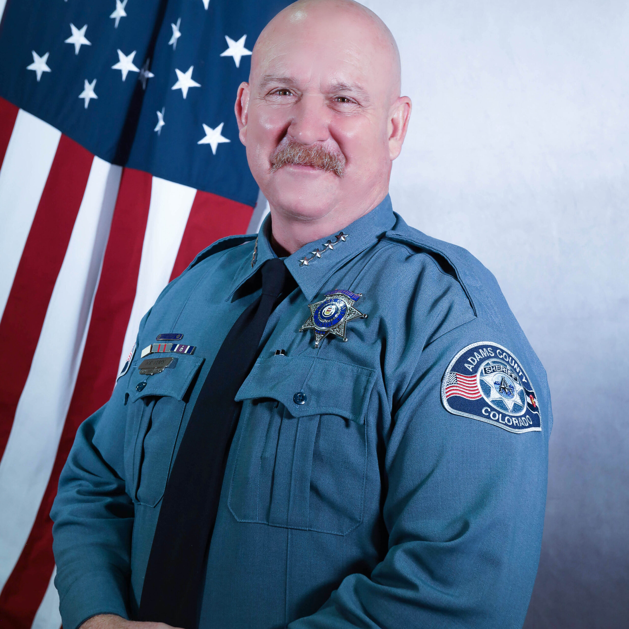 Sheriff Gene Claps in uniform standing in front of the American flag